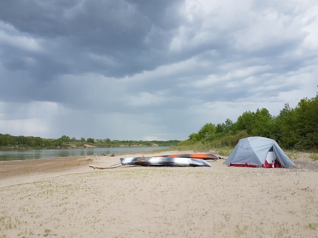 A tent and kayaks sit along a riverbank