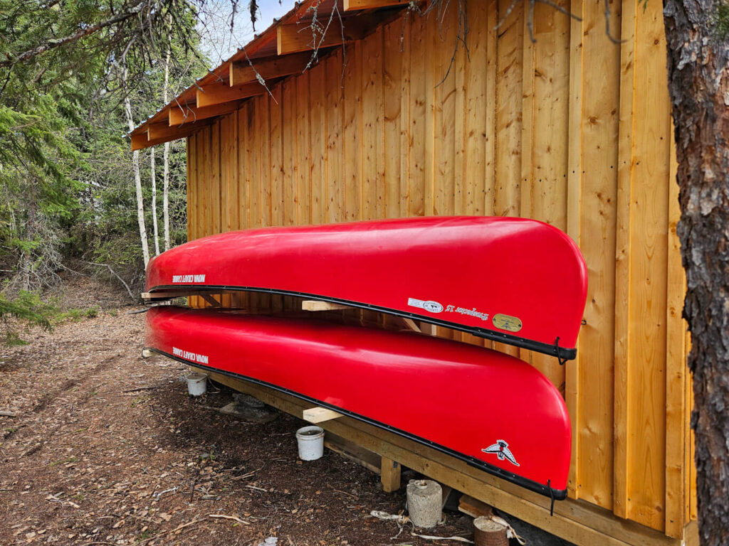 Two red canoes sit on racks along the side of a wood building