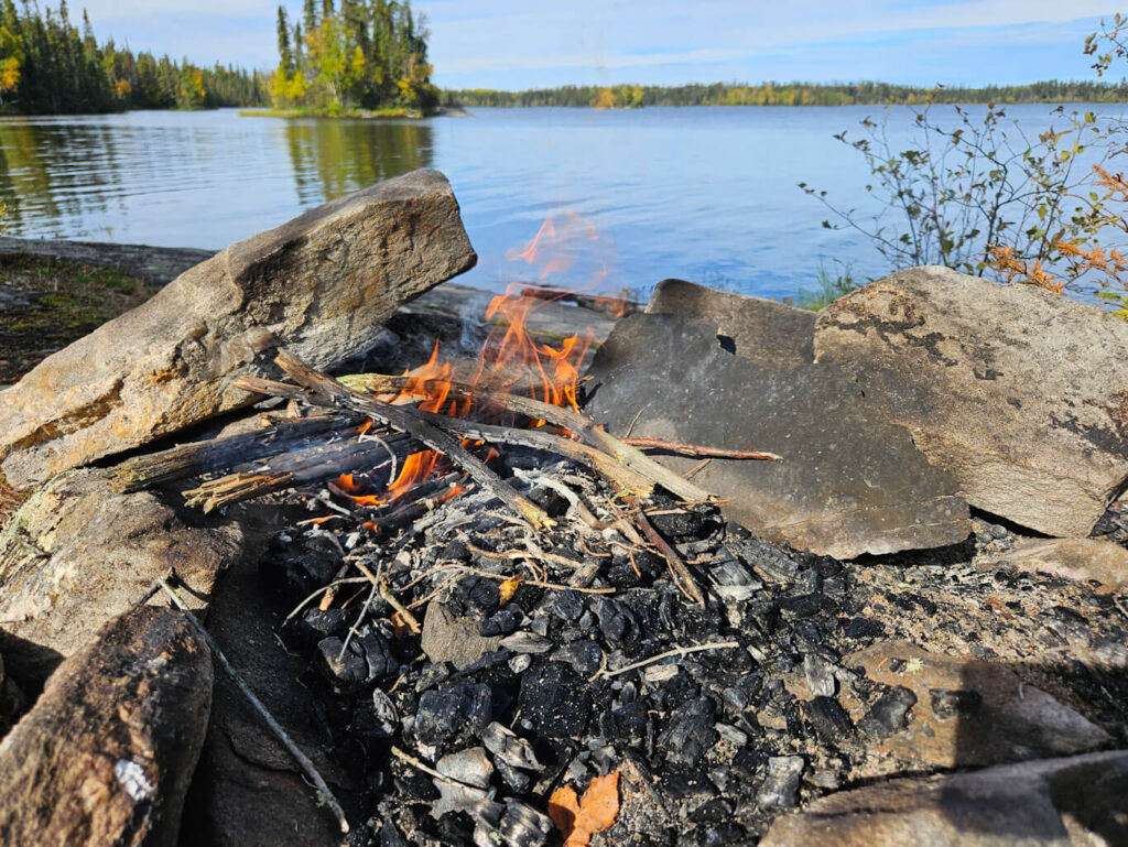 A small campfire burns in a pit beside a lake