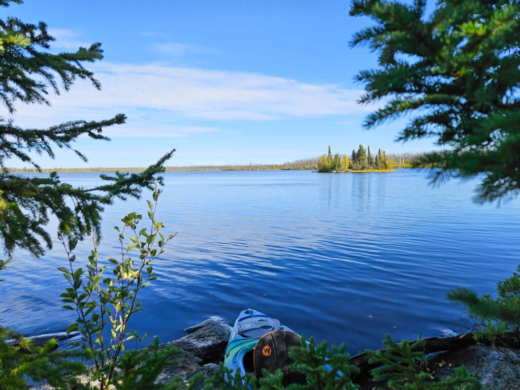 A kayak sits on the shore of a lake in the fall