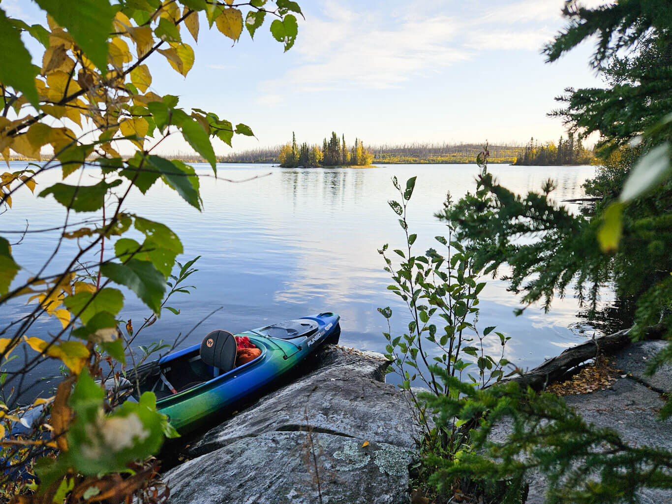 A kayak sits on the shore of a lake in the fall.